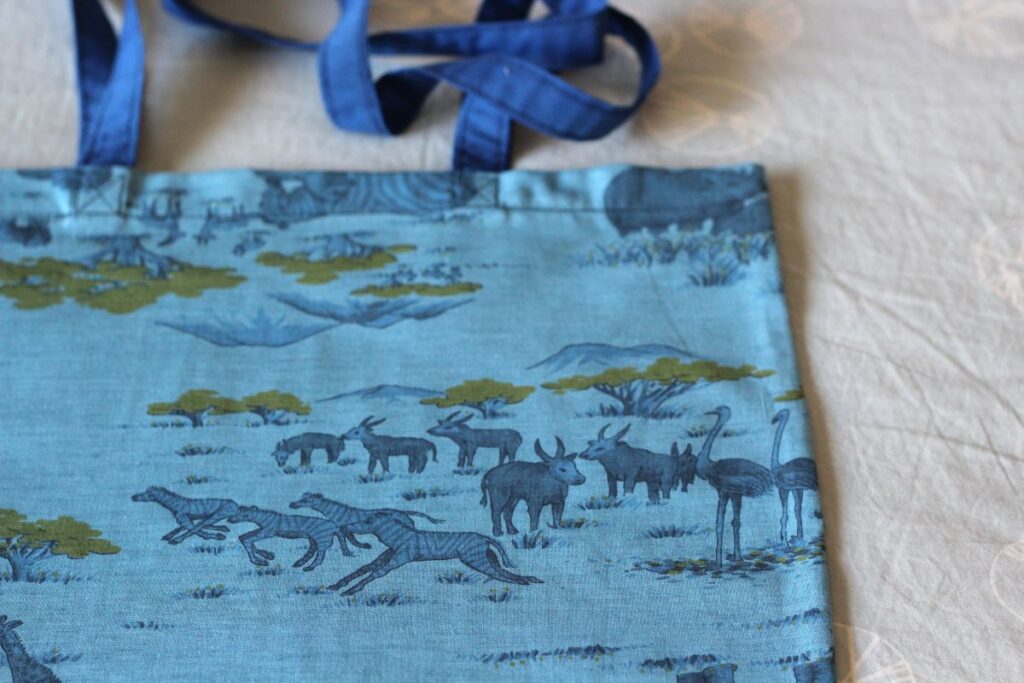 A bright blue tote bag with shoulder strap, with African animals in the vintage material design.