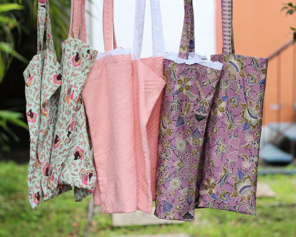 Six tote bags made from a free sewing pattern, hanging in a row in a garden.