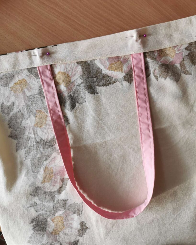 The top hem of a handmade should bag tote, with handle pinned in place ready for sewing.
