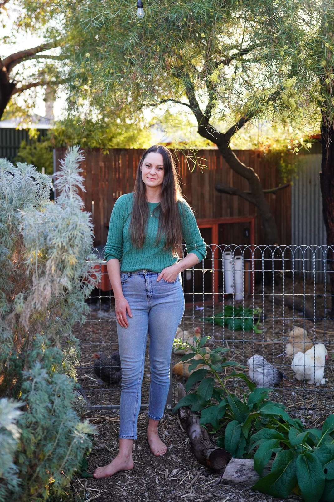 Koren Helbig (who runs Digital Marketing Coaching sessions) standing in her permaculture backyard, with pekin bantam chickens roaming in the background.