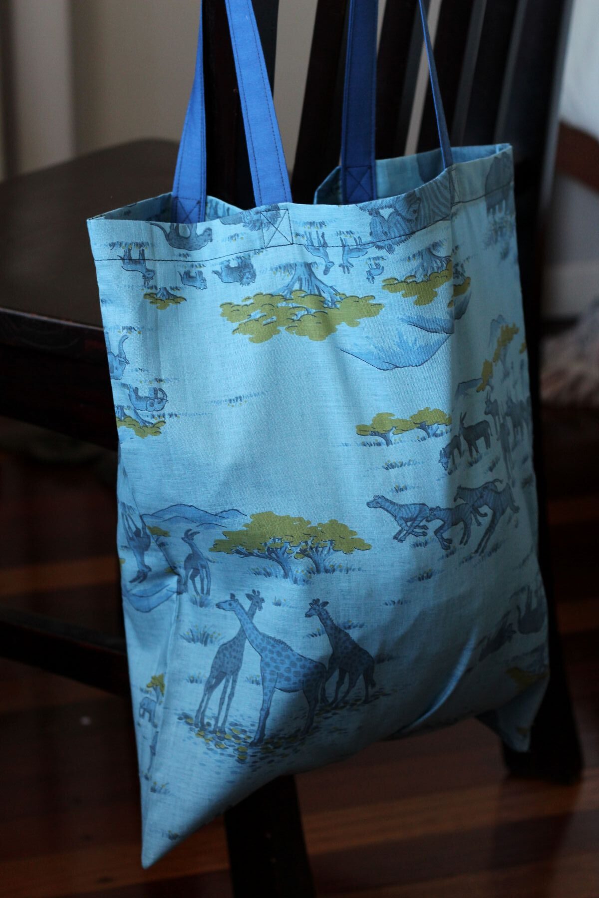 A bright blue tote bag with shoulder strap, with African animals in the vintage material design.