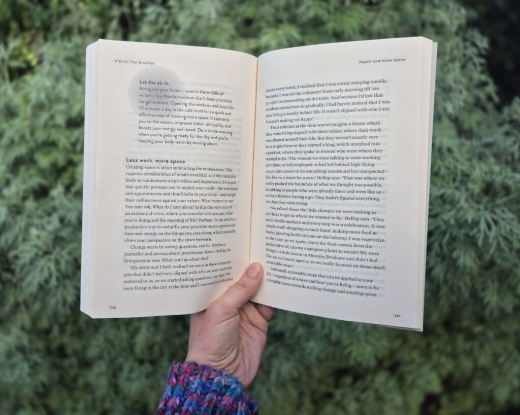 A white hand holding the book, A Brain That Breathes, open to the pages that include quotes from Koren Helbig.