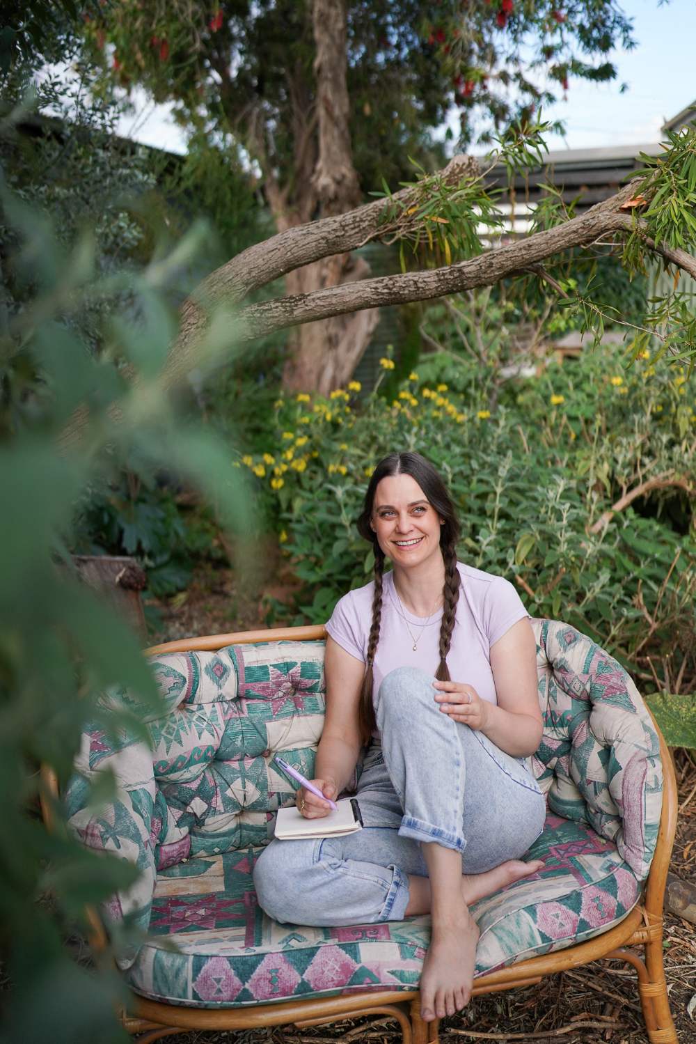 Permaculture Marketing founder Koren Helbig sitting on a retro cane couch in a lush native garden.